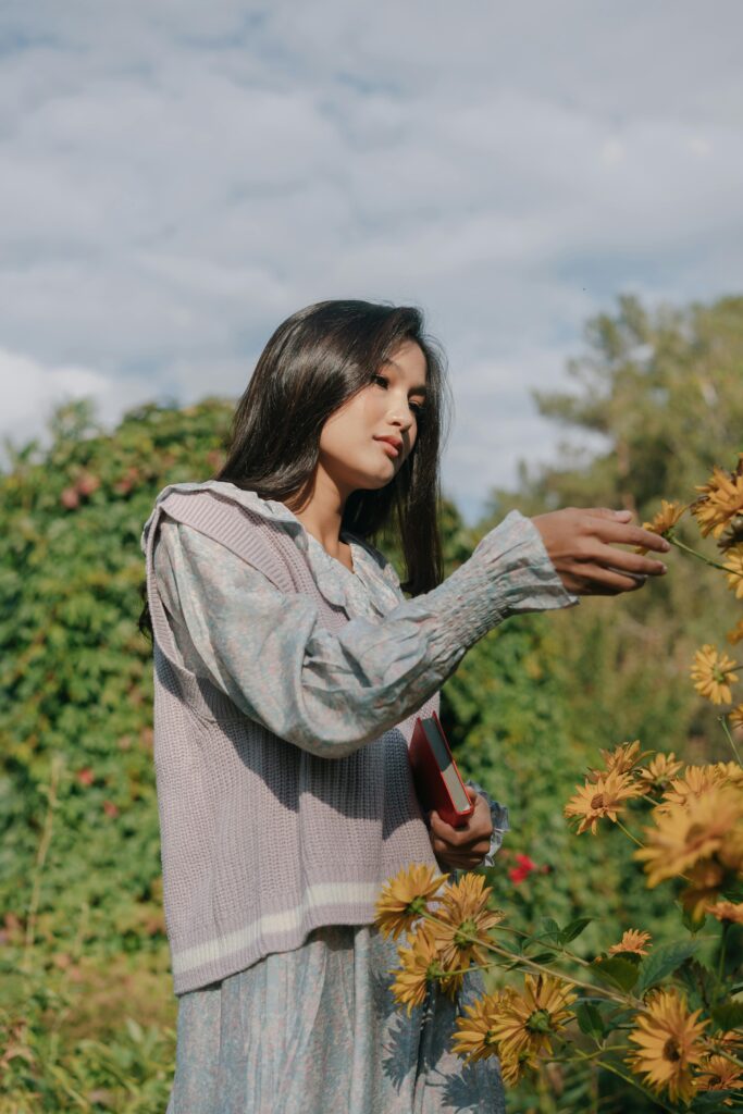Asian woman with long hair picking yellow flowers in a lush garden setting.
